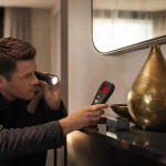 Tecnico che cerca una telecamera nascosta con torcia e rilevatore in una stanza